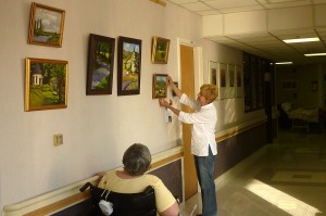 A resident watches as artist Remington Restivo finishes putting up an exhibit of her original oil paintings  at LNRC.